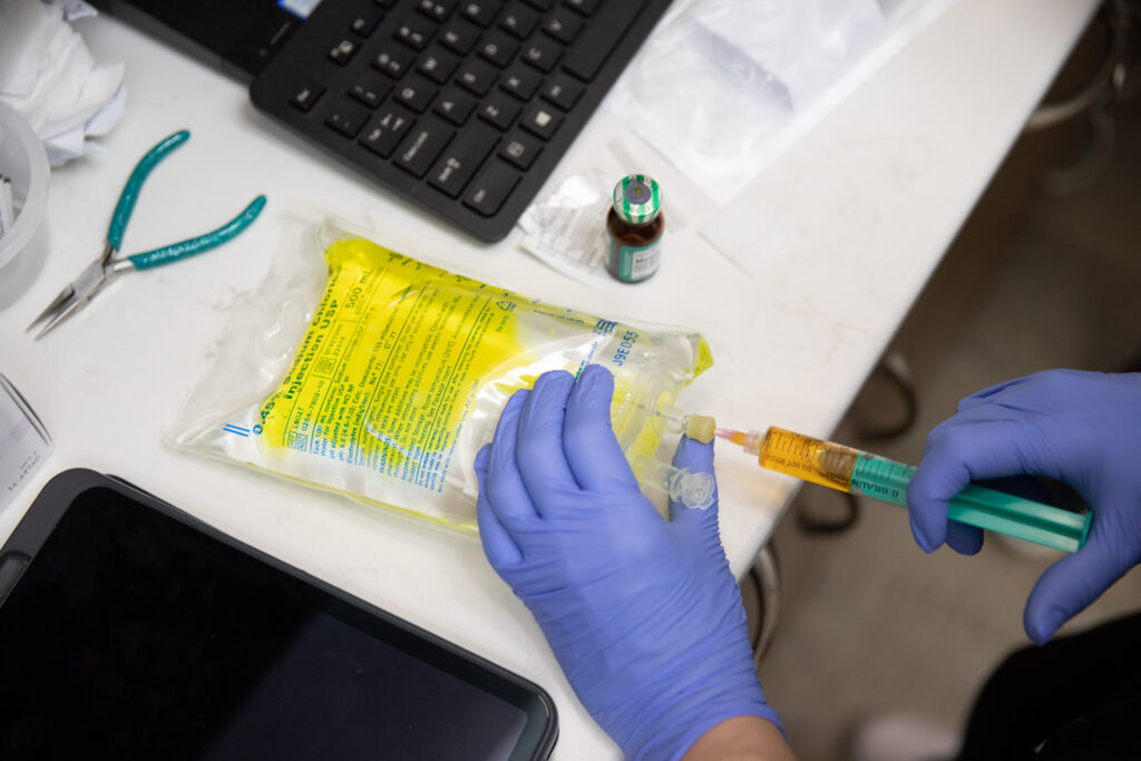 A close-up of a provider using a syringe to inject a vitamin add-on into an IV bag used at a wellness center in Nashville.