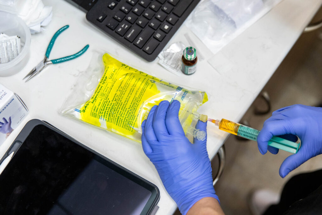 A medical professional wearing blue gloves prepares an IV bag on a desk for a patient's immune system booster in Nashville