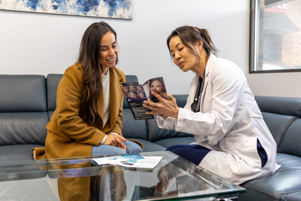 Sitting on the leather sofa in front of a glass table, an Intravenous Solutions provider points to information on a brochure for a fit female client. They're discussing IV drips for athletic recovery in Nashville.