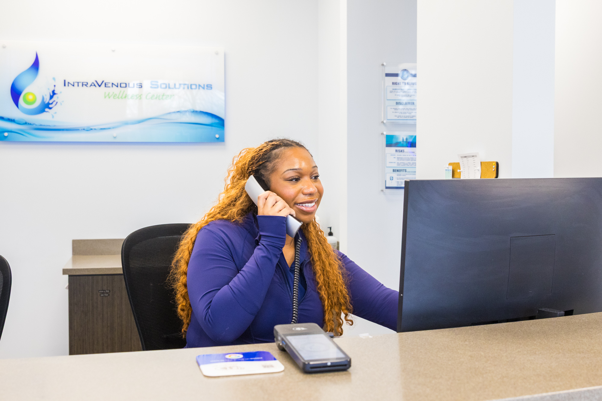An employee at IntraVenous Solutions sits at a desk in the front lobby while she smiles and answers the phone.
