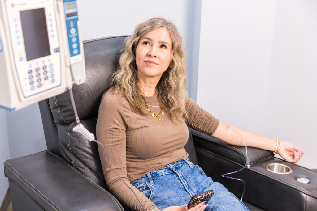 A woman sits in a reclining chair looking upwards at an IV machine as she receives migraine relief in Nashville.