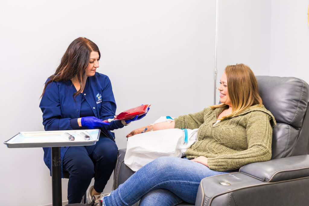 A registered nurse holds a red-colored ozone infusion bag, with a client seated in front of her receiving joint pain therapy in Nashville.