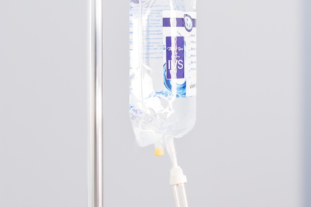 Close-up of an IV fluid bag, with IntraVenous Solutions branding, hanging from a stand, with tubing connected and clear liquid visible inside.