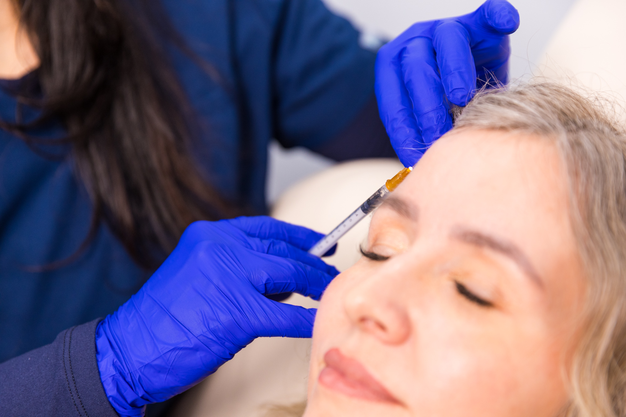 A gloved nurse injects Botox in a female client's forehead.