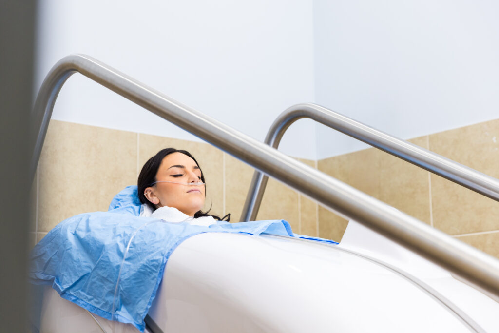 A woman rests in the HOCATT sauna with her head exposed, eyes shut, and a nasal cannula in her nose.