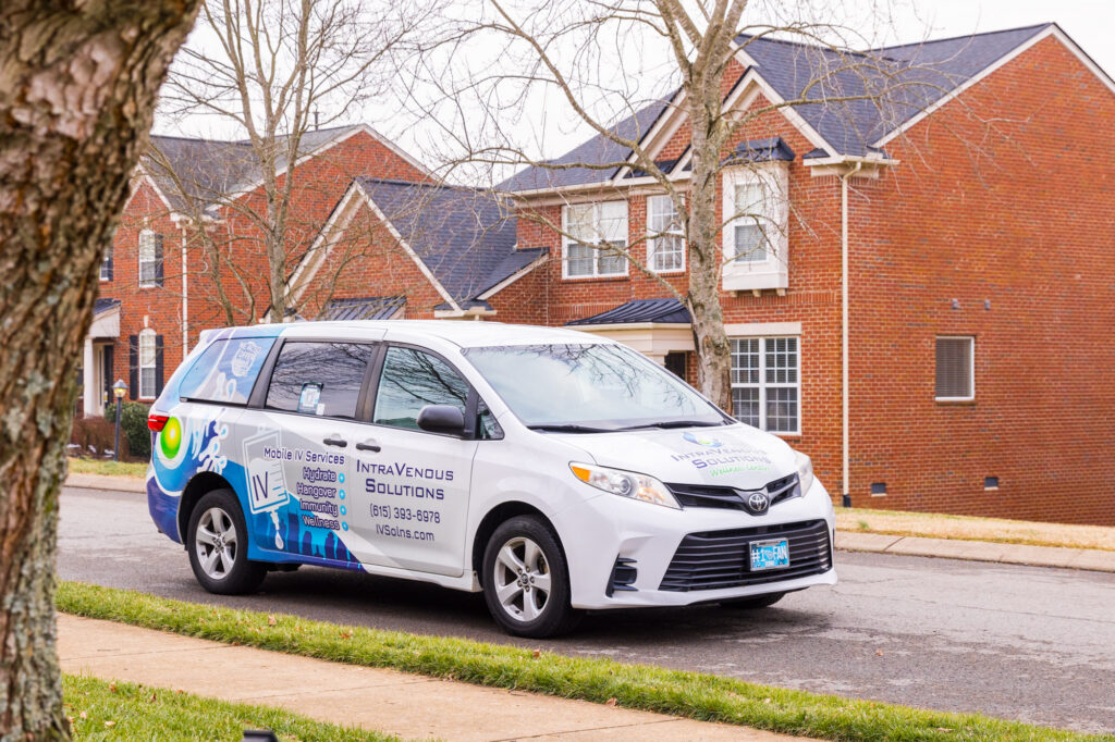 A white mobile service van for IntraVenous Solutions parked on a suburban street, ready to provide IV therapy at home.