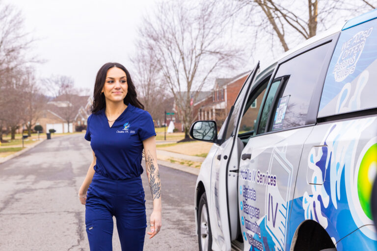 A nurse in navy scrubs walks beside a branded mobile IV van.